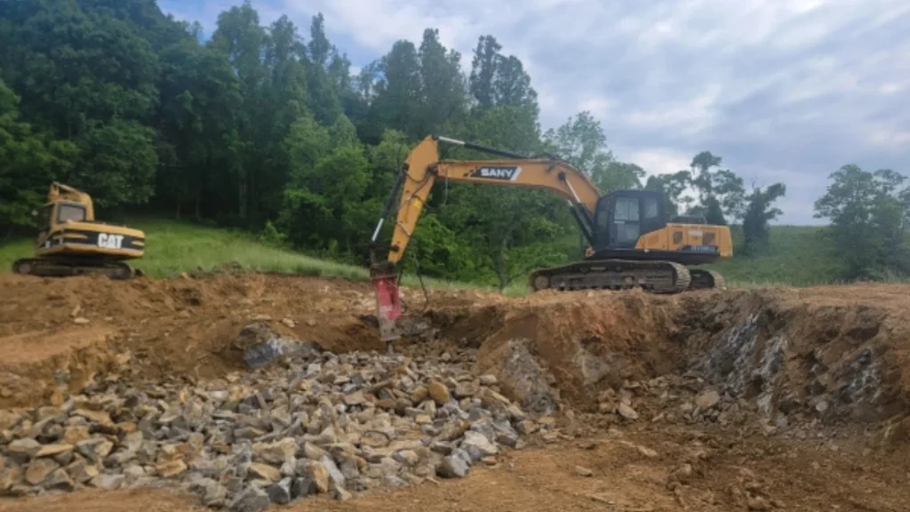 Large excavator digging during site development in a wooded area by J. Hunziker Asphalt Paving