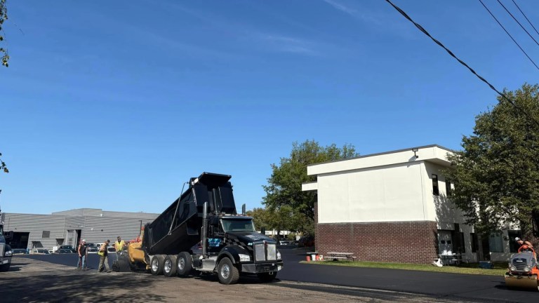 Heavy paving equipment and dump trucks working on a commercial asphalt job in Glenville, NY
